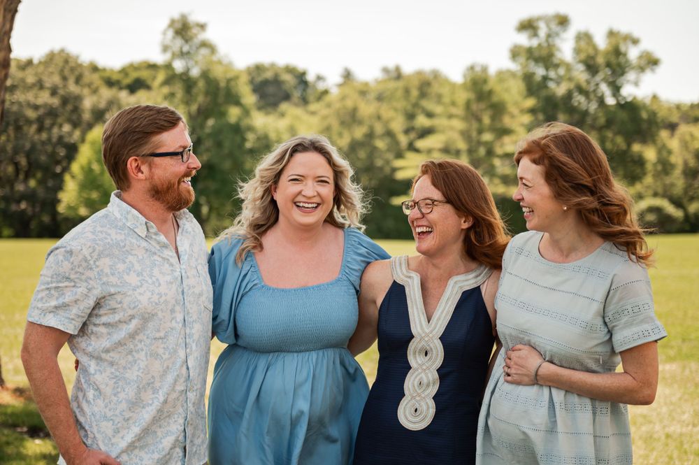 Group of four adults smiling and laughing together outdoors on a sunny day.
