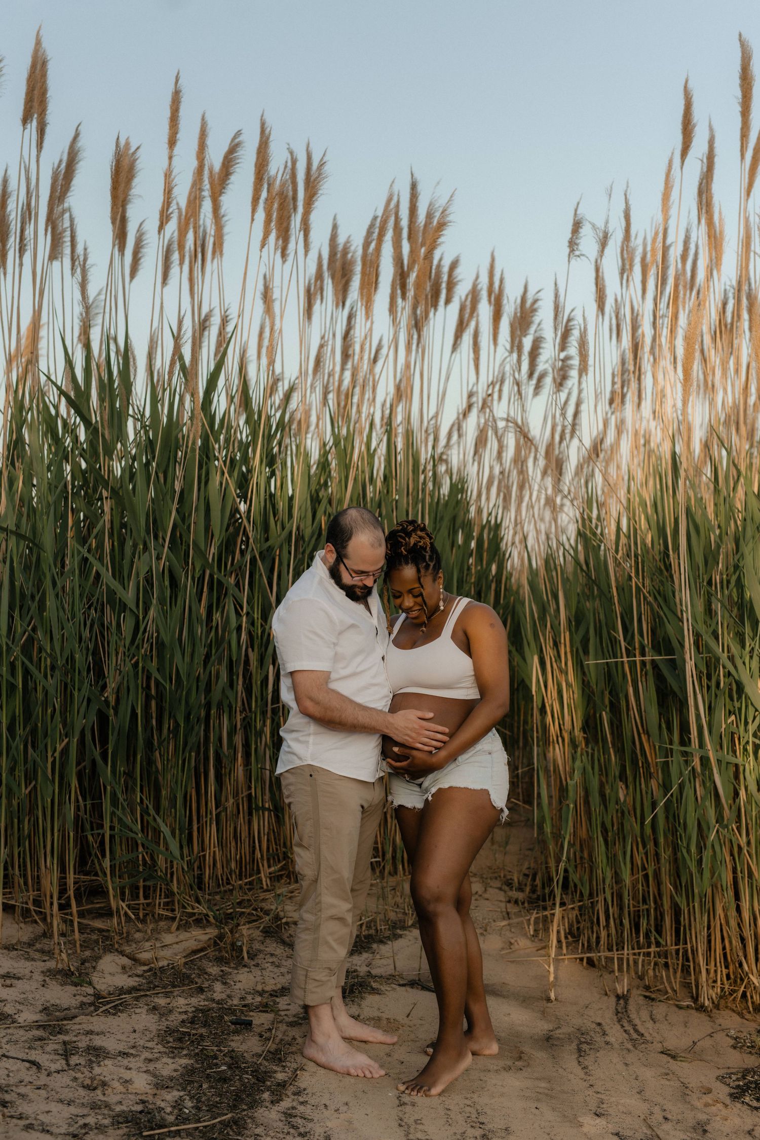 Romantic couple embrace among tall beach grass during golden hour.