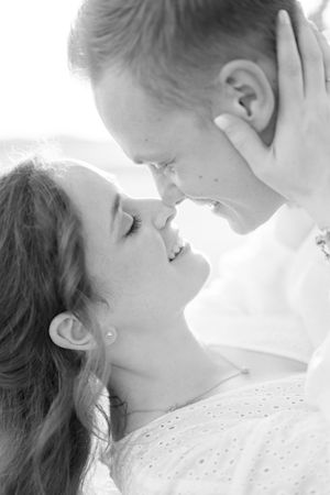 Black and white close-up of smiling couple leaning in for a kiss in soft light.