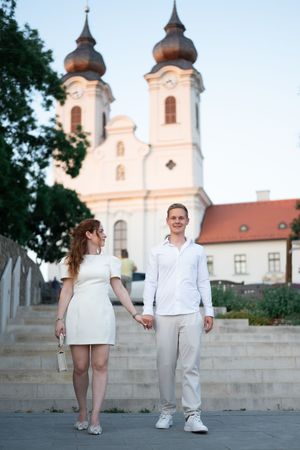 Couple holding hands on steps with historic baroque church with copper domed towers behind them.