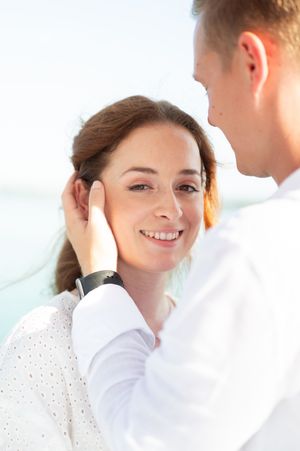 Romantic close-up of smiling woman as man gently holds her face with both hands outdoors.