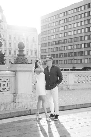 Black and white photo of a stylish couple posing together on a sunny urban bridge in the city.