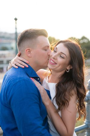 Man kissing smiling woman on the cheek at golden hour on a bridge in Budapest.