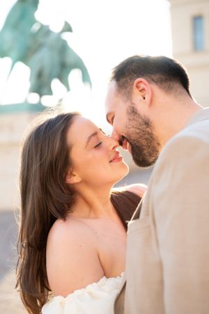 Romantic couple nearly kissing in warm sunlight with bronze equestrian statue in the background.