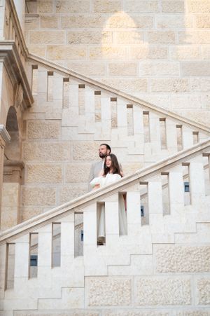 Elegant couple walking down grand limestone staircase inside a beautiful historic European building.