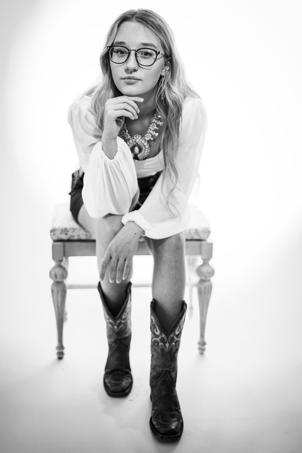 Black-and-white fine art portrait of a young woman seated on a bench during a studio session in Mountain Home, Arkansas