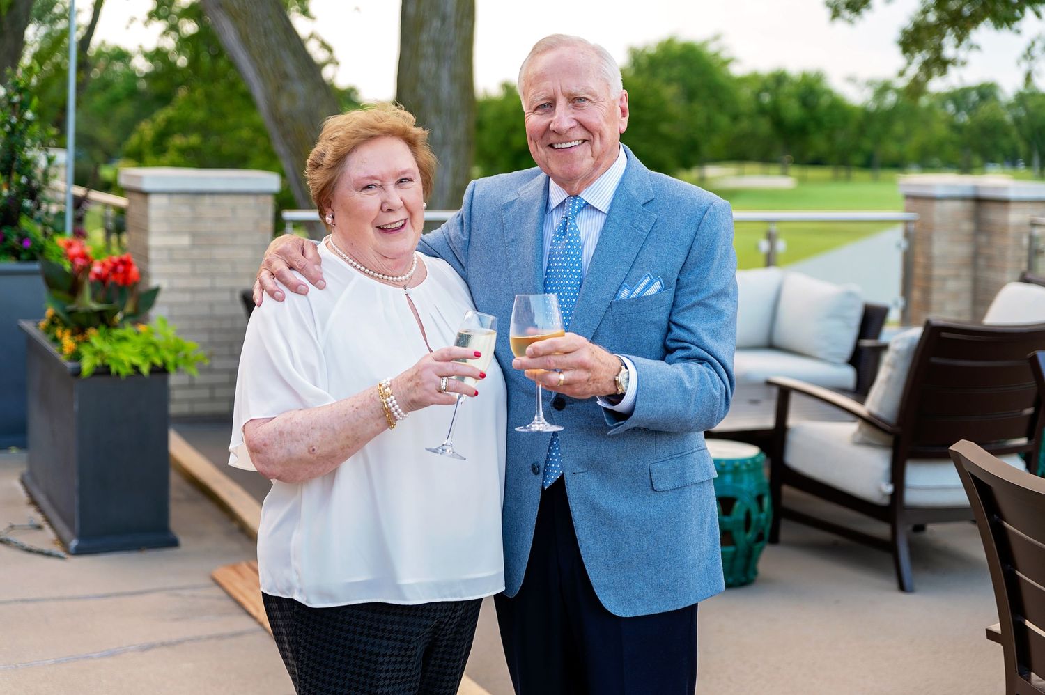 Couple enjoying drinks together on outdoor patio with garden decor at country club.