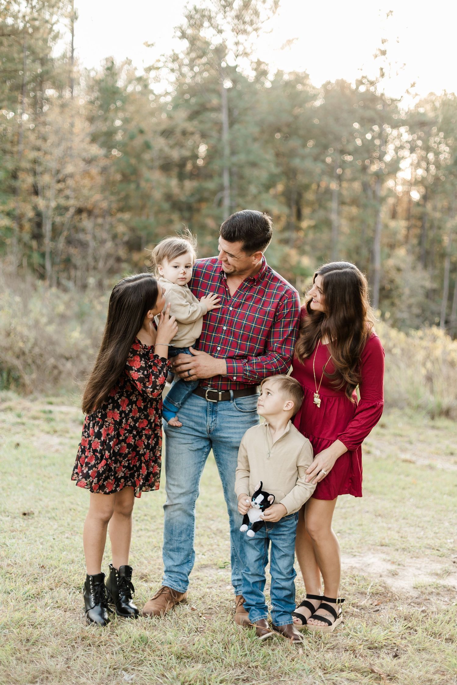 Family shares playful moments together during outdoor photo session in pine forest.