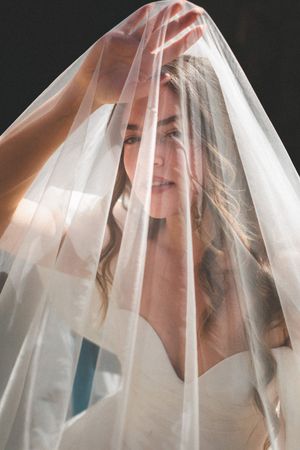 Ethereal artistic portrait through sheer white veil creating dreamy romantic effect in natural lighting.