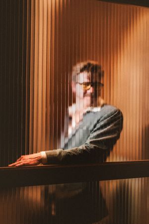 A cinematic sequence showing a figure in warm lighting behind vertical window blinds creating a film noir atmosphere.