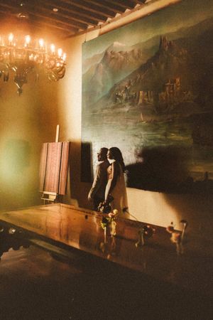 A romantic candlelit room with a large landscape painting and chandelier creates an elegant atmosphere at a historic venue.