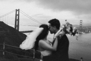 Couple embraces near the Golden Gate Bridge in San Francisco during a cloudy day with moody atmosphere.