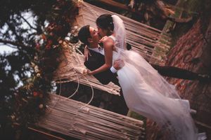 A couple in wedding attire poses together on rustic wooden stairs surrounded by autumn foliage.