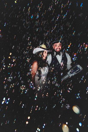 A couple celebrates at their wedding reception with bubbles floating through the dark atmosphere creating a magical effect.