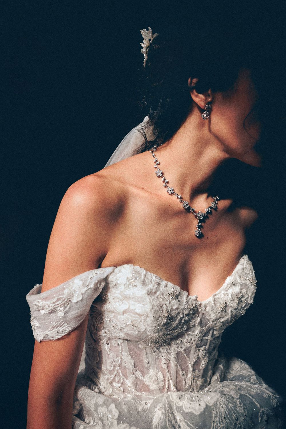 Close-up details of a white lace wedding dress bodice with off-shoulder design against dark background.