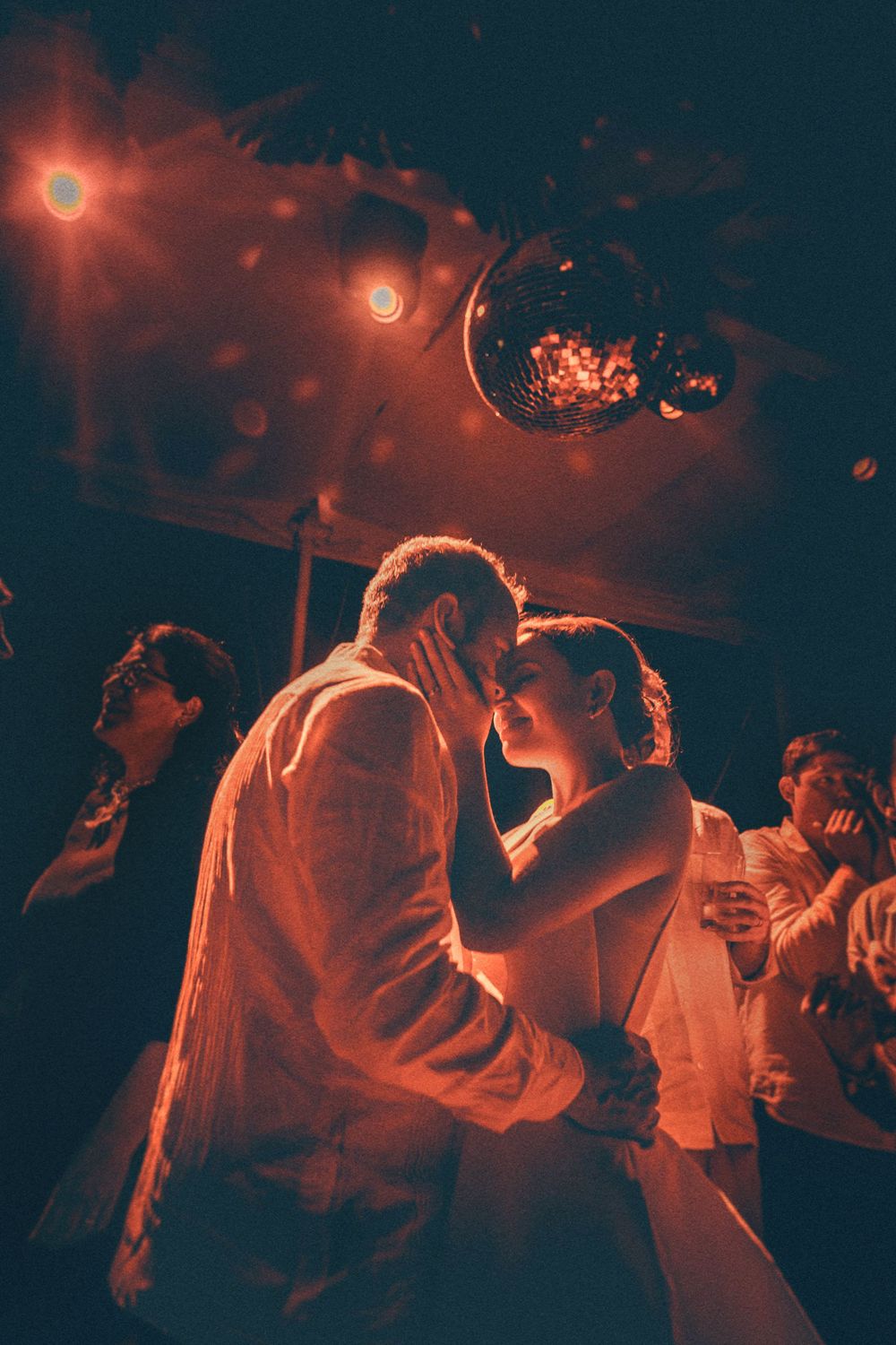 Silhouettes of people dancing in a nightclub illuminated by warm red lighting and disco balls.
