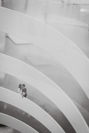 Black and white minimalist architectural photograph showing curved amphitheater seating with two small figures at the far end.