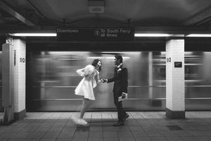 Motion blur captures commuters and trains moving through a monochromatic subway station platform.