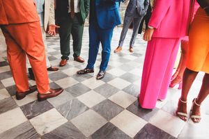 People in bright orange and pink traditional clothing stand on a checkered floor at a cultural gathering.