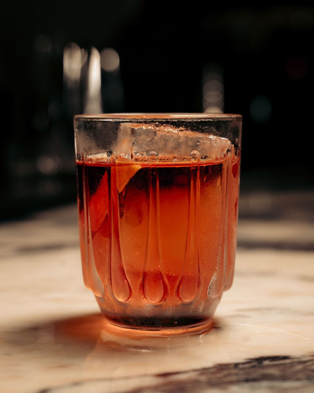 Amber cocktail with large ice cube in vintage ribbed glass on marble surface.

Vancouver Canada Scene