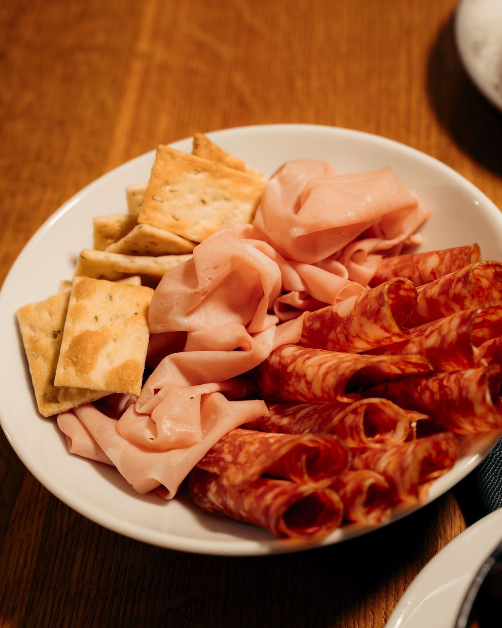 Charcuterie plate with sliced mortadella, salami, and crackers on white dish.

Vancouver Canada Scene