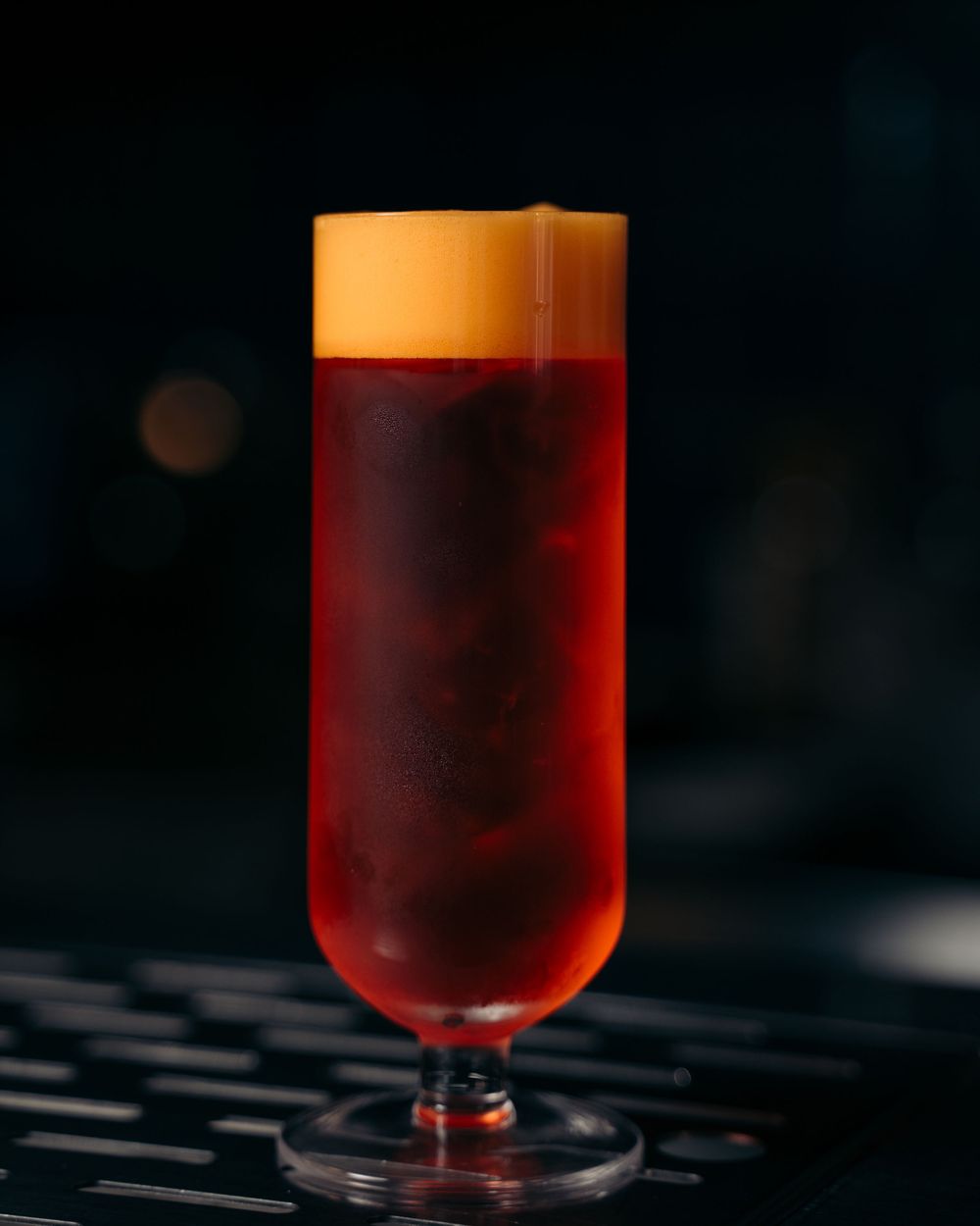 Vibrant red cocktail with orange foam top served in a tall flute glass on a dark bar.

Vancouver Scene