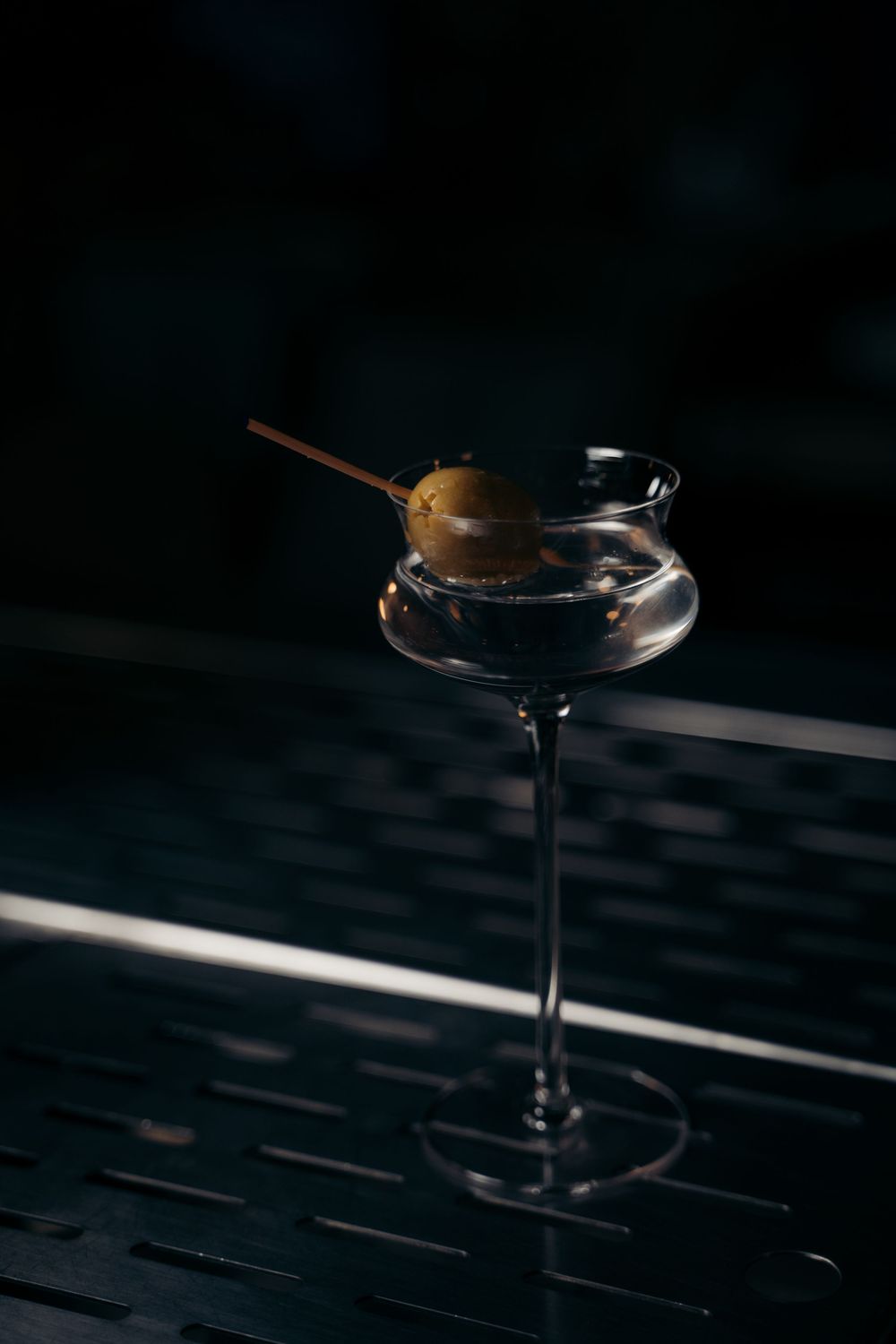 Classic dirty martini with olive garnish on a metal pick in an elegant coupe glass on a dark bar.

Vancouver Scene
