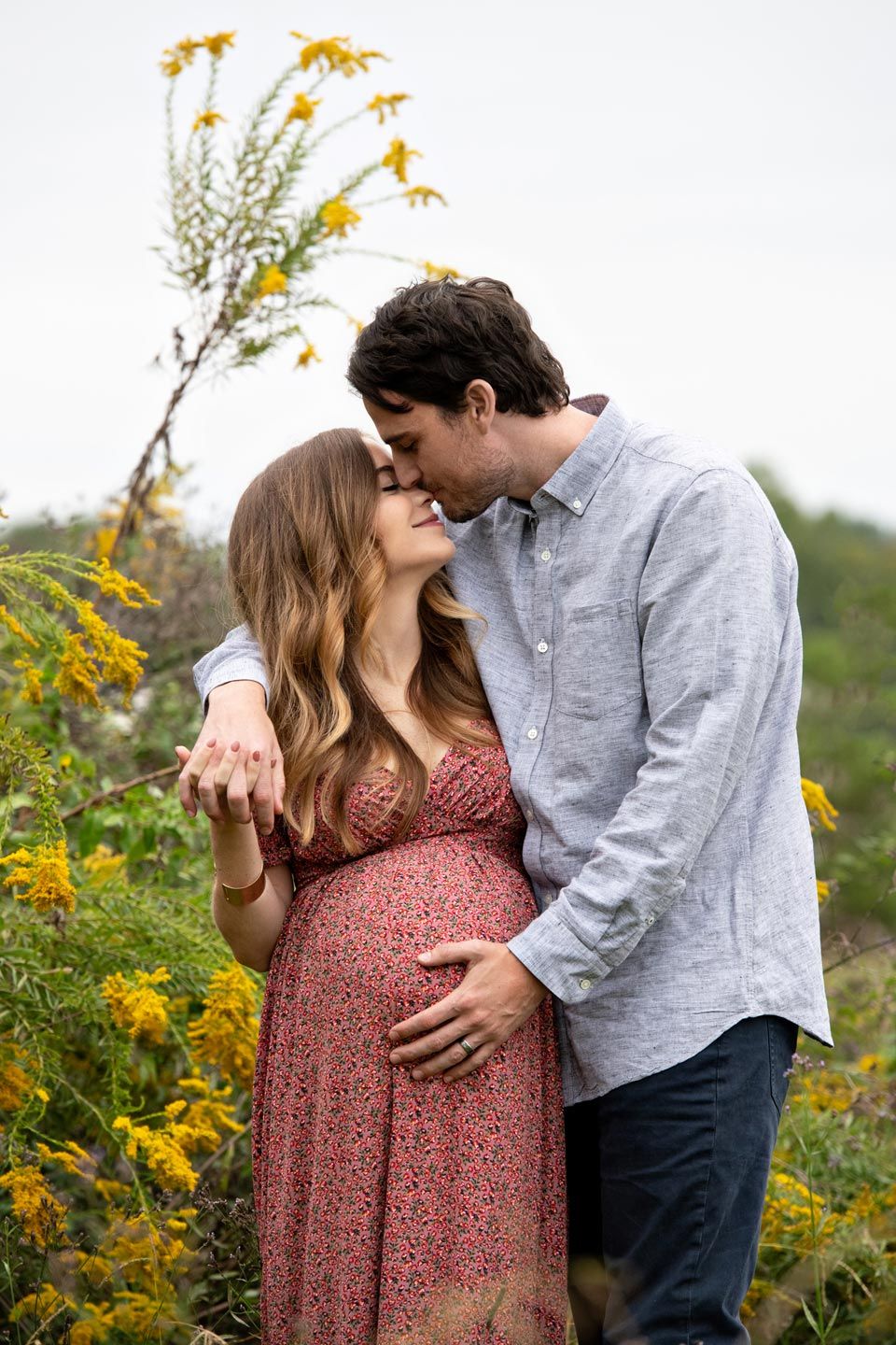 An intimate maternity portrait of a couple embracing in a field of yellow wildflowers.