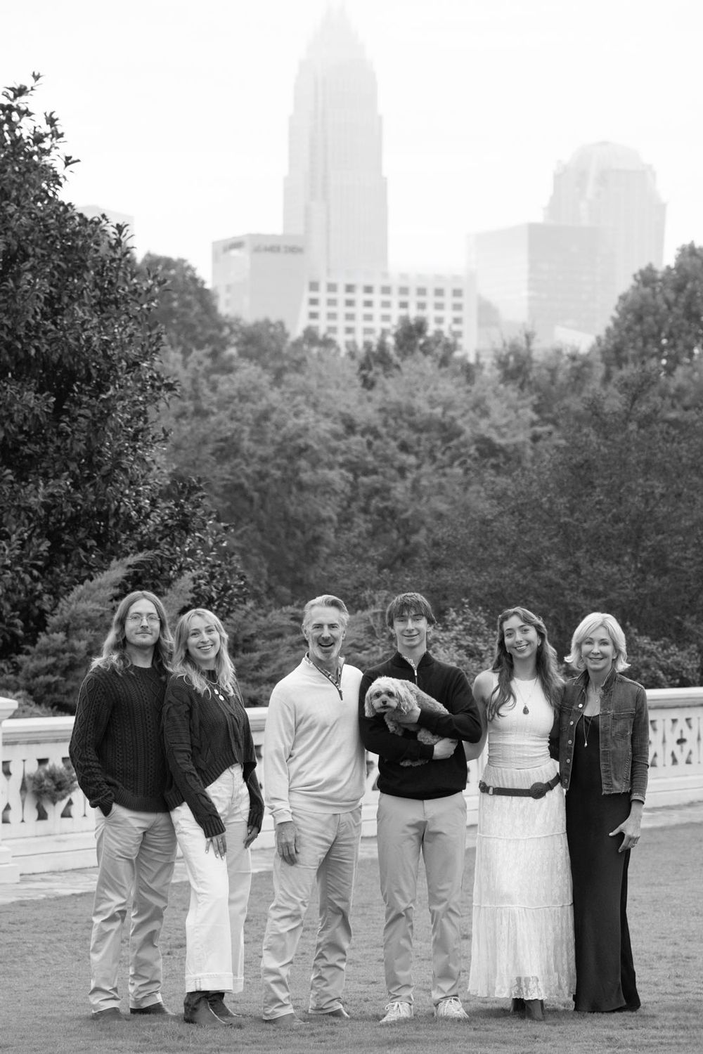A black and white group portrait in front of a city skyline with tall buildings and trees in the background.