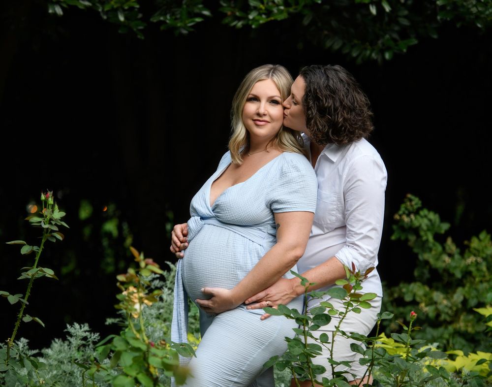 A couple shares a tender moment outdoors surrounded by lush greenery and natural light.