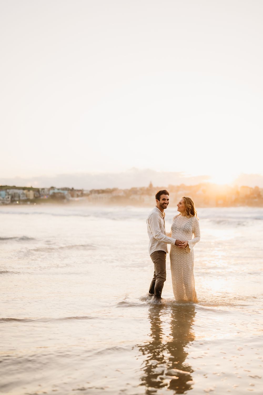 A couple having fun splashing in the ocean during their maternity shoot