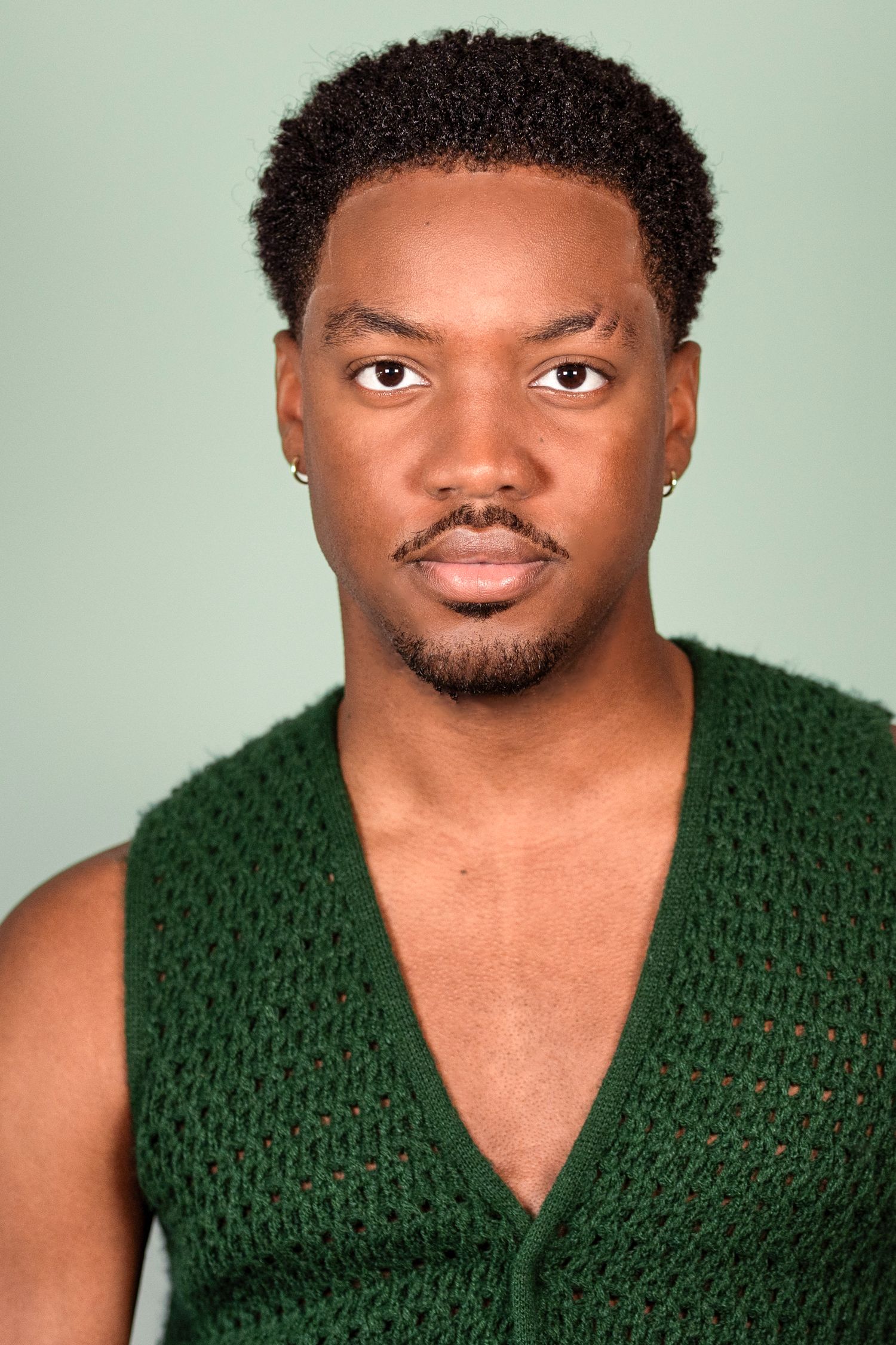 Studio headshot wearing green knit vest against mint green background.