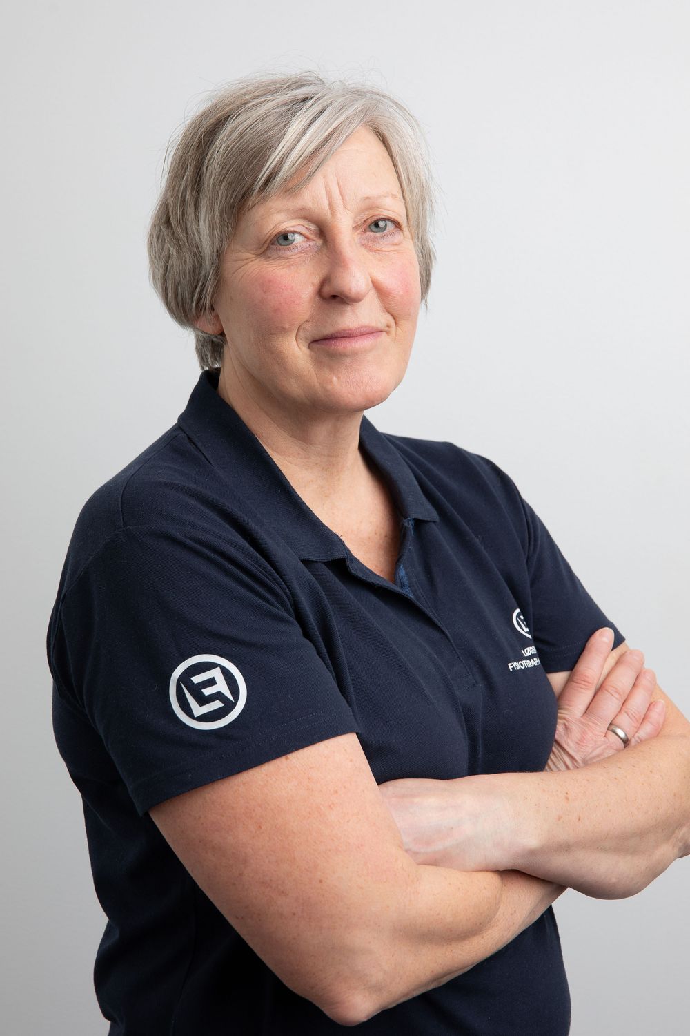 Woman in navy polo shirt with crossed arms, short gray hair, professional portrait photo.