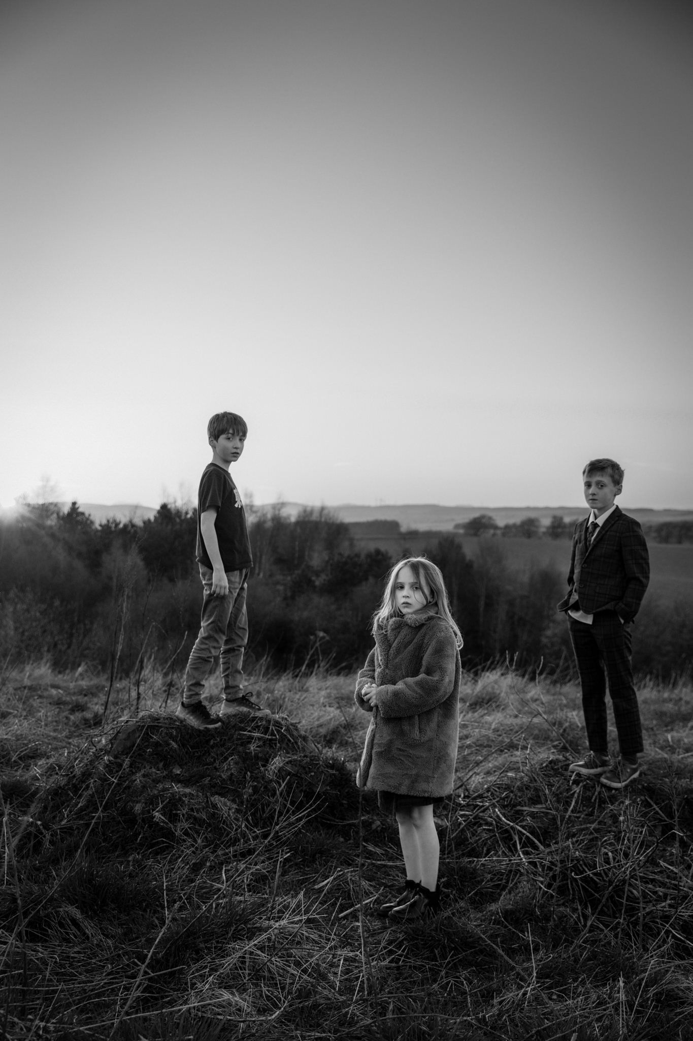Three children standing in a grassy landscape, photographed in black and white