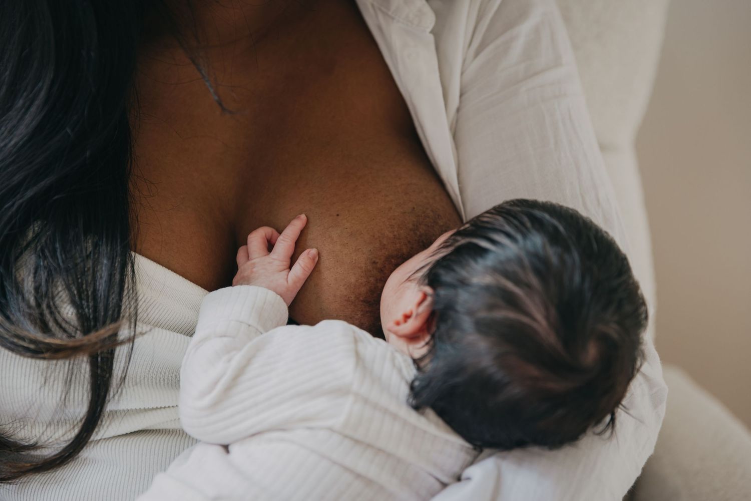 Un bébé pose la main sur le sein de sa jeune maman lors d'une séance d'allaitement, sous l'oeil d'une photographe pro