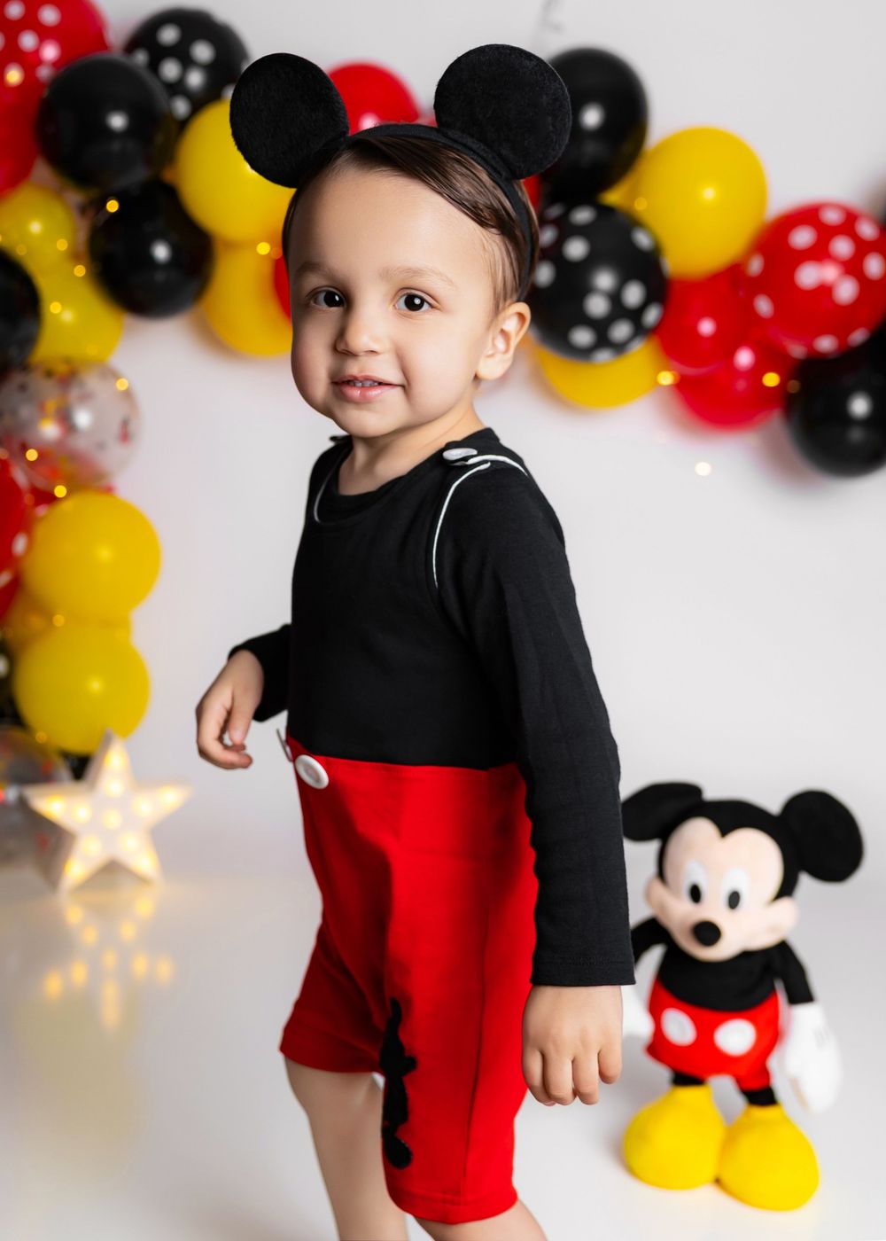 Mickey Mouse themed birthday party decorations with balloons in red, yellow and black polka dot patterns against white background.