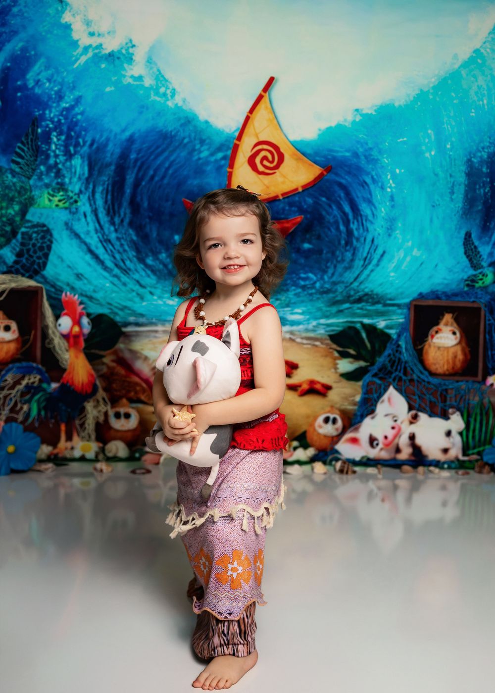 Moana toddler photoshoot with colorful costume poses against an underwater-themed backdrop with sea creatures and waves.