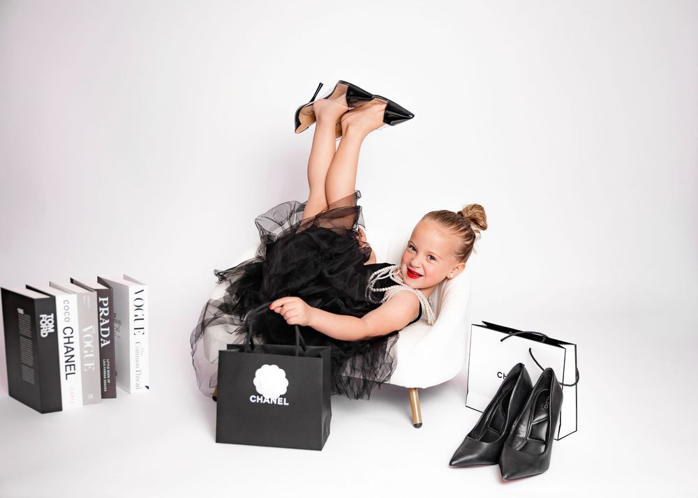 Toddler photoshoot in black and white sits with shopping boxes and bags scattered around them on a white background.