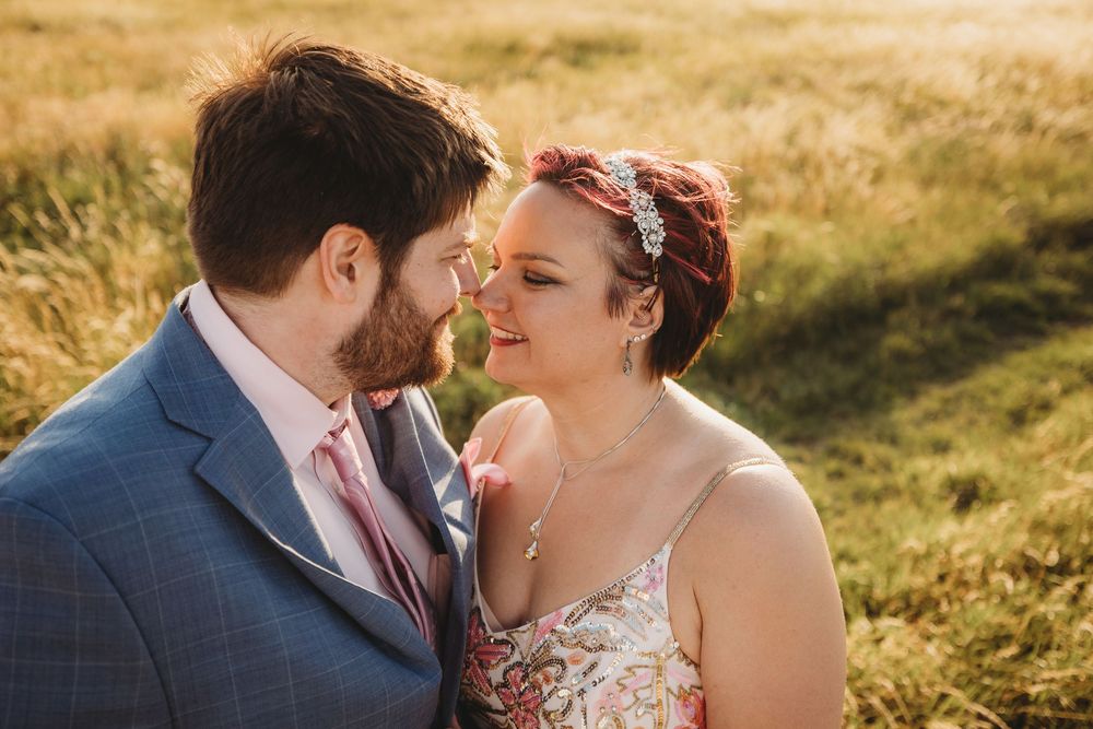 Couple sharing an intimate moment in a coastal field during golden hour with sea cliffs in background.