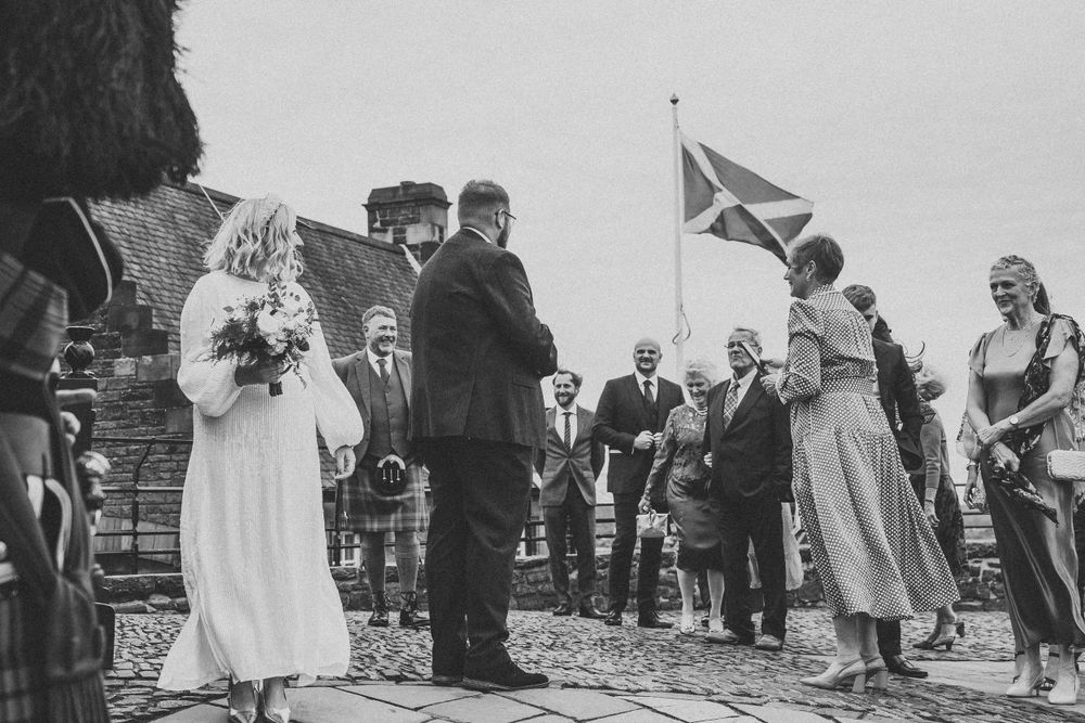 Black and white photo of a wedding group gathered on stone steps with a Scottish flag.