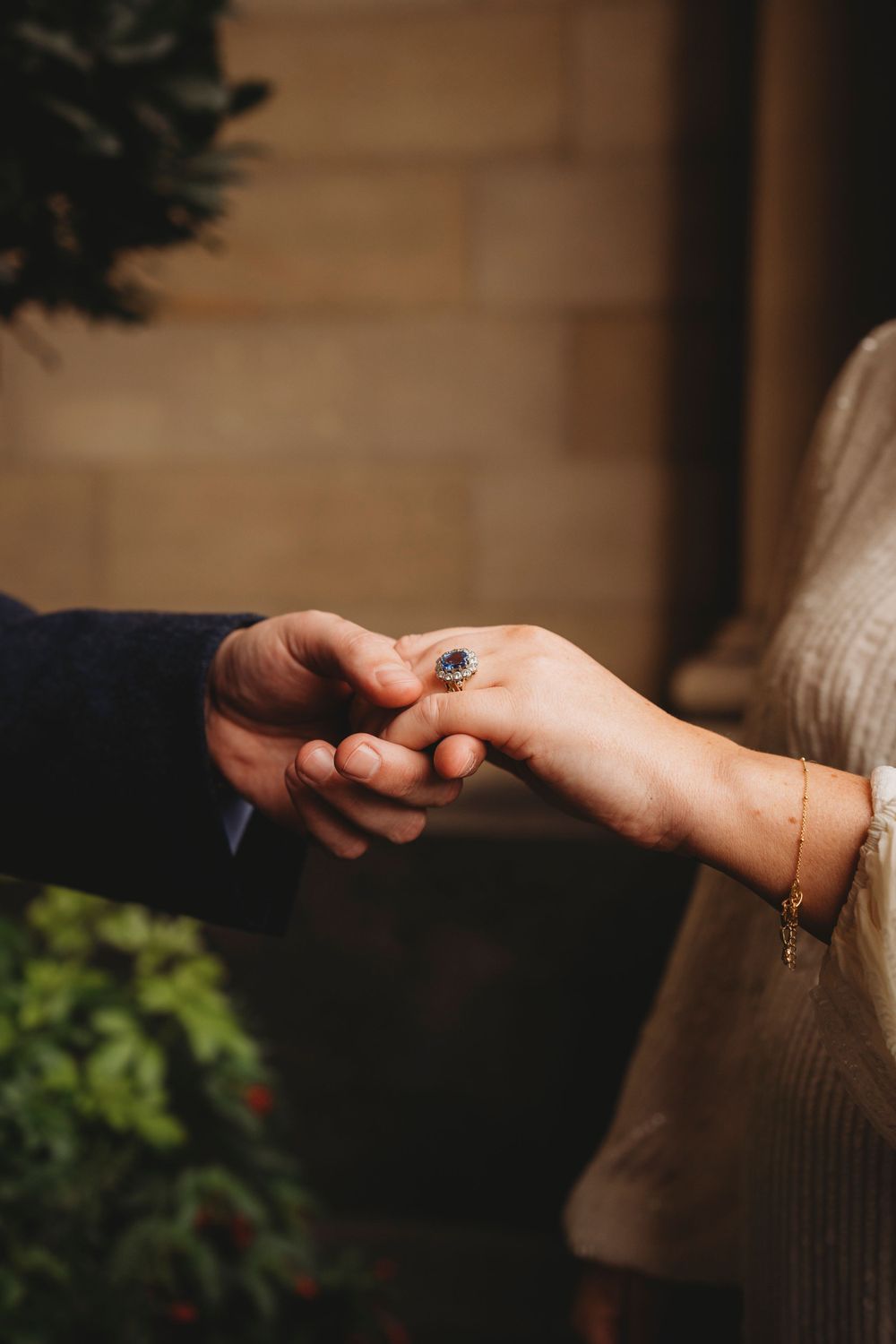 Close-up of hands exchanging a wedding ring with a delicate bracelet visible.
