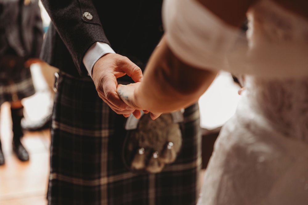 Close-up shot of hands during a wedding ceremony with traditional Scottish kilt visible.