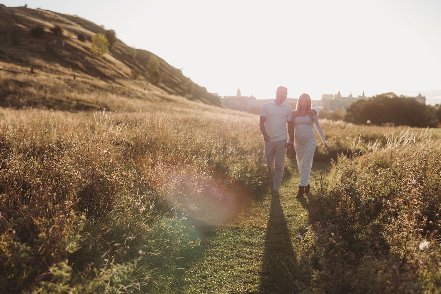 Silhouettes of two people walking through a sunlit meadow during golden hour.