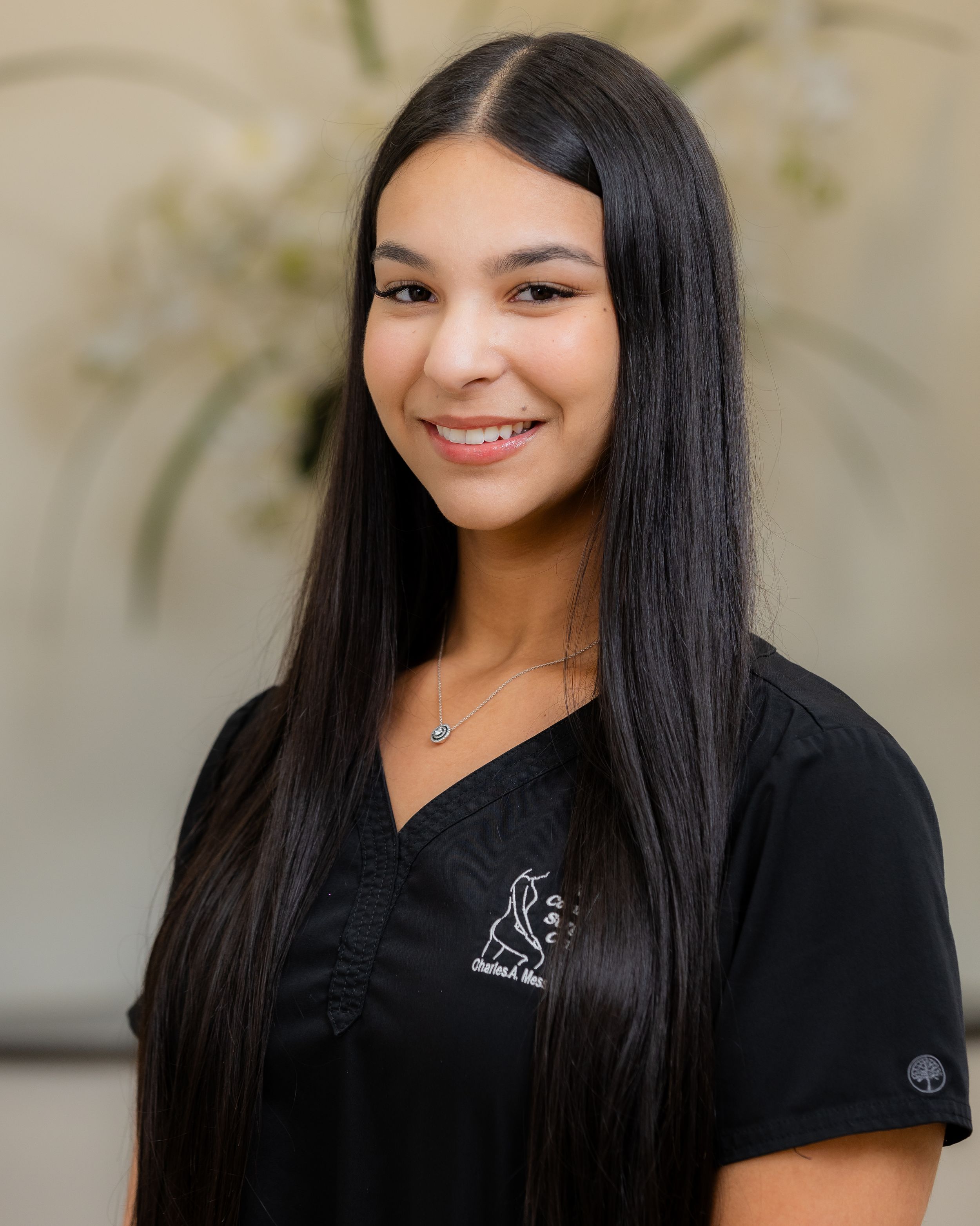 Team member in black scrubs smiles warmly against neutral background in professional healthcare portrait series.
