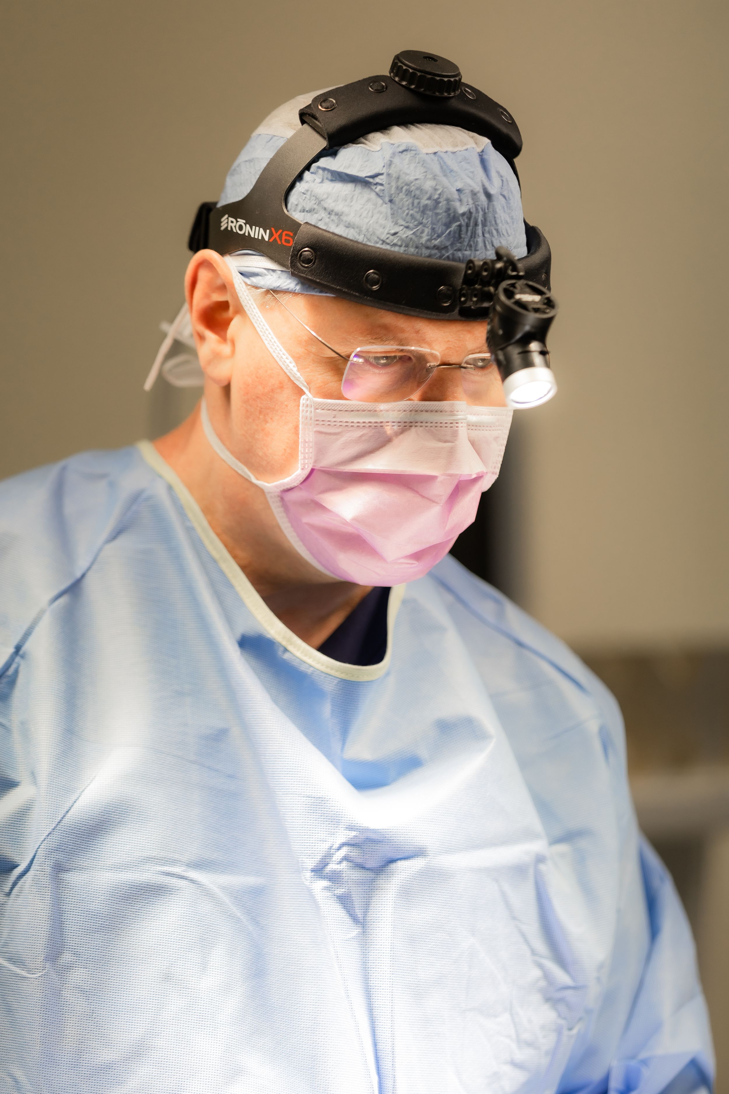 Medical professional wearing surgical scrubs, face mask and protective headgear during procedure.