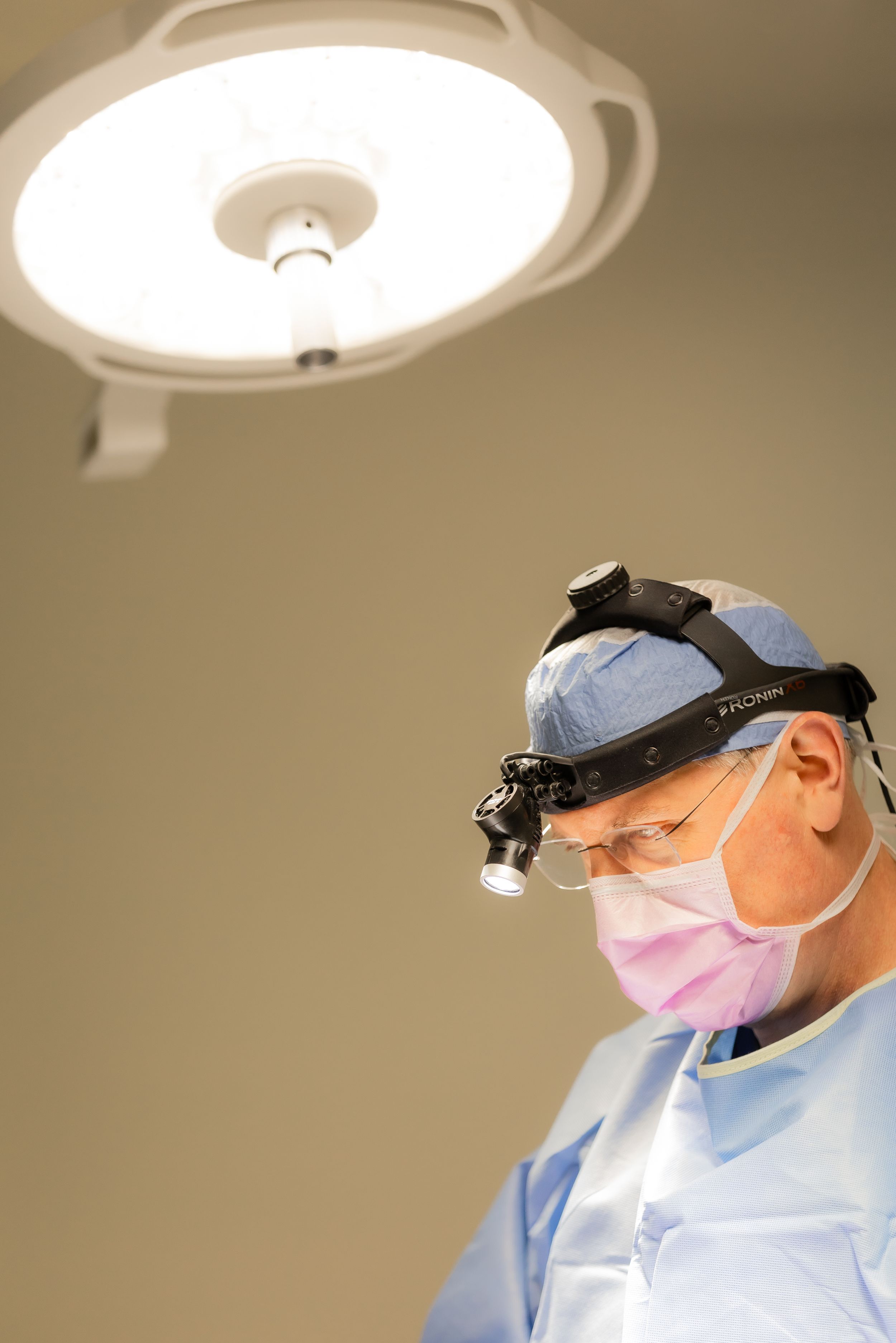 Medical professional wearing surgical mask and headlamp performing examination in clinical setting.
