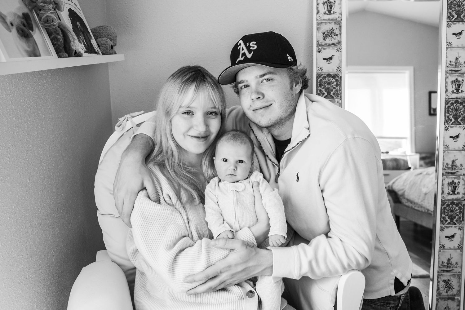 Black and white family portrait with infant in casual home setting.