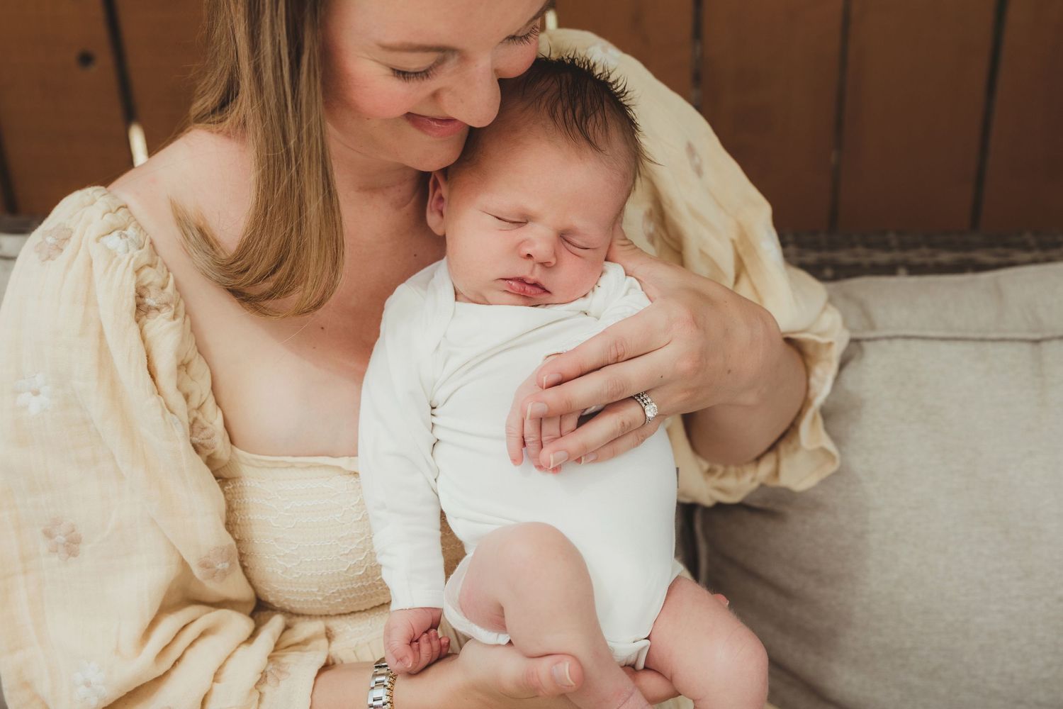 Tender moment with newborn in white onesie being held in cream colored setting.