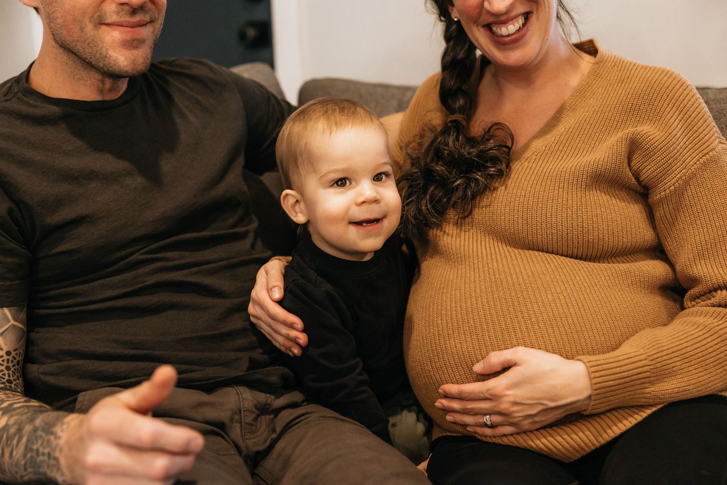 Family moment with toddler sitting between parents on couch while expecting second child.