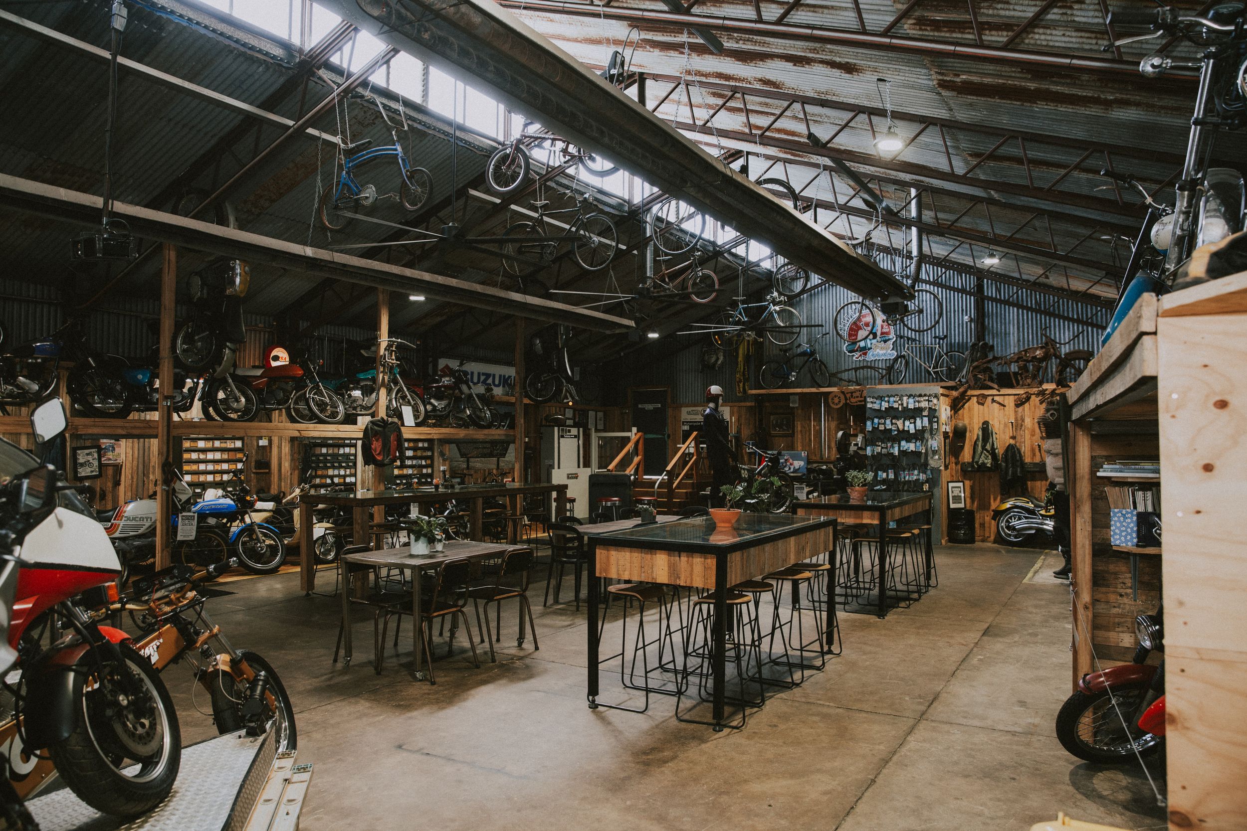 Panoramic view of a motorcycle workshop interior with bikes lined up and tools scattered throughout the space.